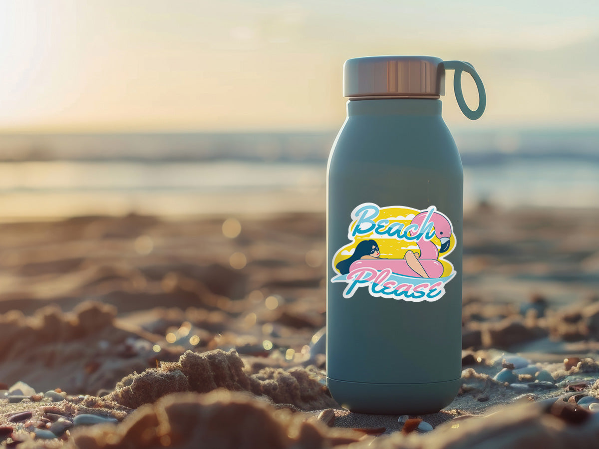 A water bottle sitting on a sandy beach at sunset, featuring a colorful sticker with the text “Beach Please” and a playful flamingo float design. The background shows blurred ocean waves, enhancing the tropical and relaxed vibe.