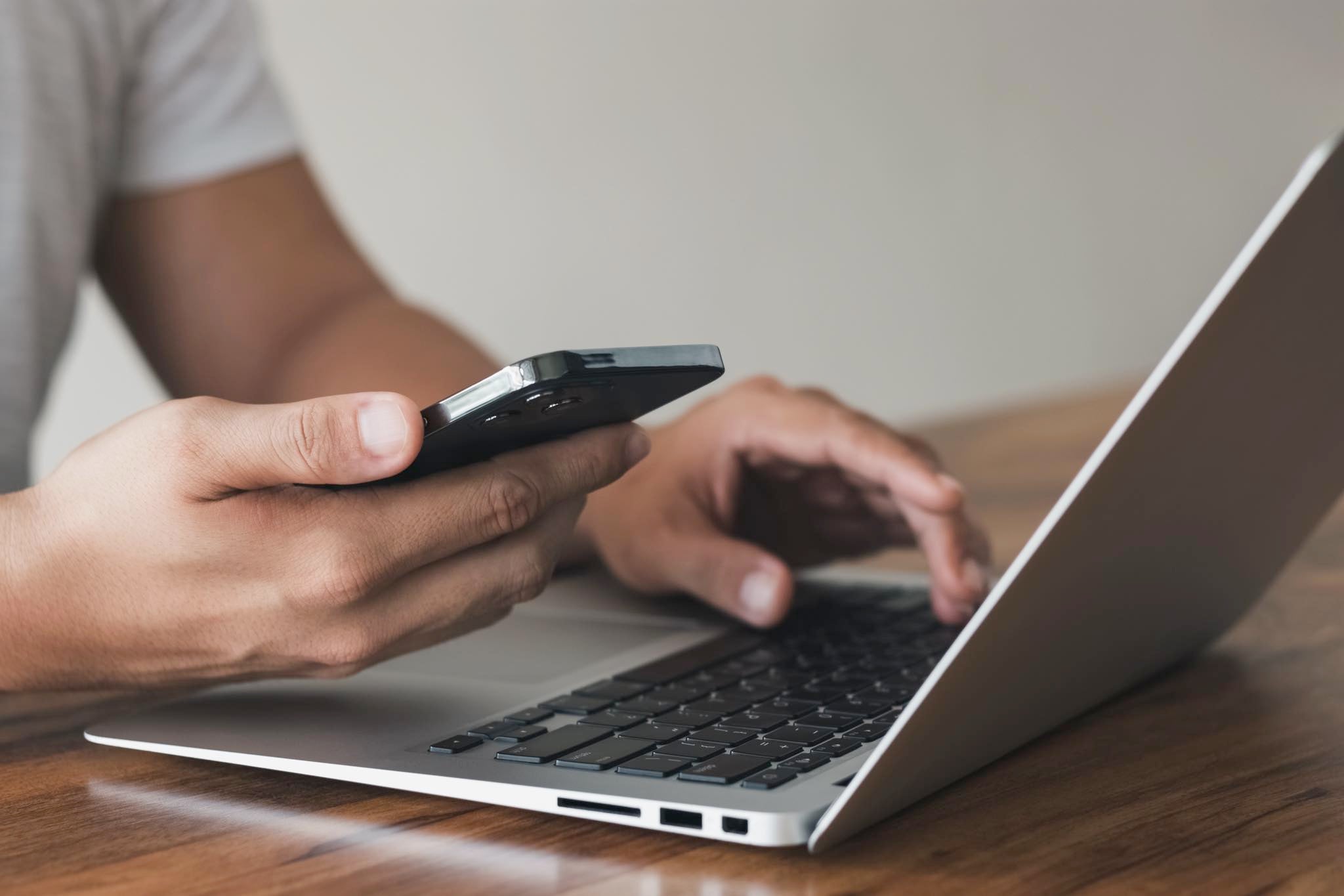 Man holding an iPhone in his hand and working on Macbook.